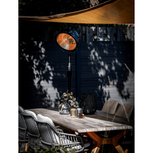 Zwarte staande heater met draaibare kop bij een tuintafel.